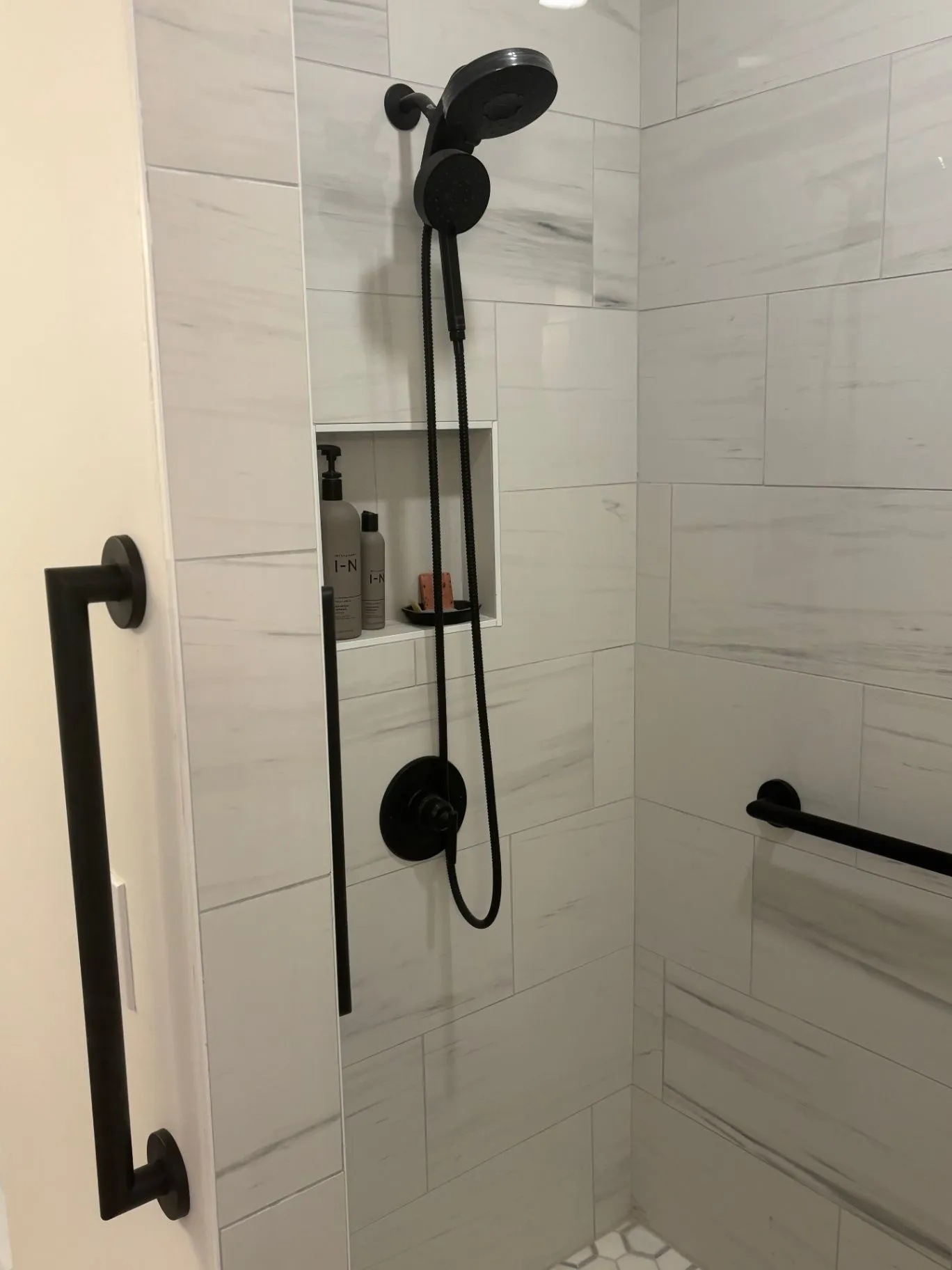 Black-finish shower installation with a handheld shower, recessed shelf, and horizontal grab bar