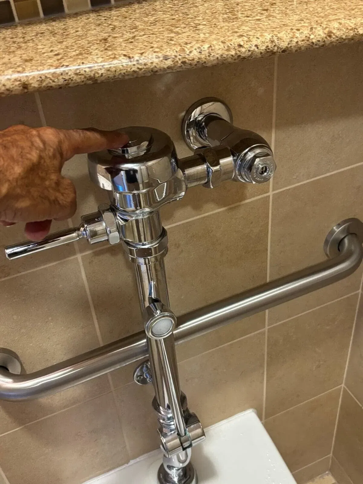 Service-context image of a technician inspecting a chrome commercial flush valve